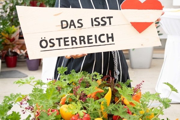 Holzschild mit einer Österreich-Flagge in Herzform und dem Text: Das isst Österreich, darunter regionales Gemüse