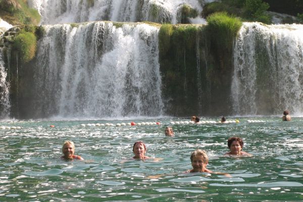 Am Foto sind 9 schwimmende Personen vor einem kleinen Wasserfall zu sehen
